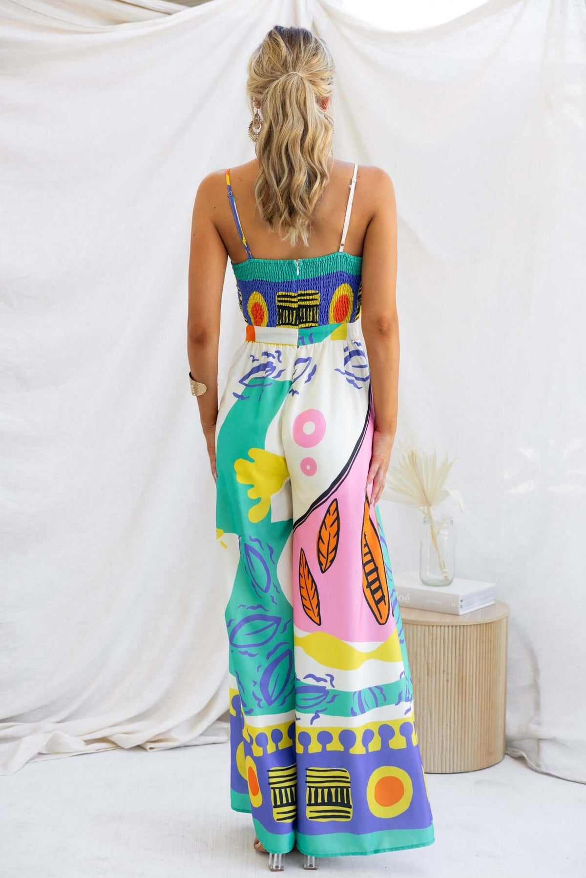 Back view of a multi-colour print Sun Dazed jumpsuit with adjustable straps and tie detail.