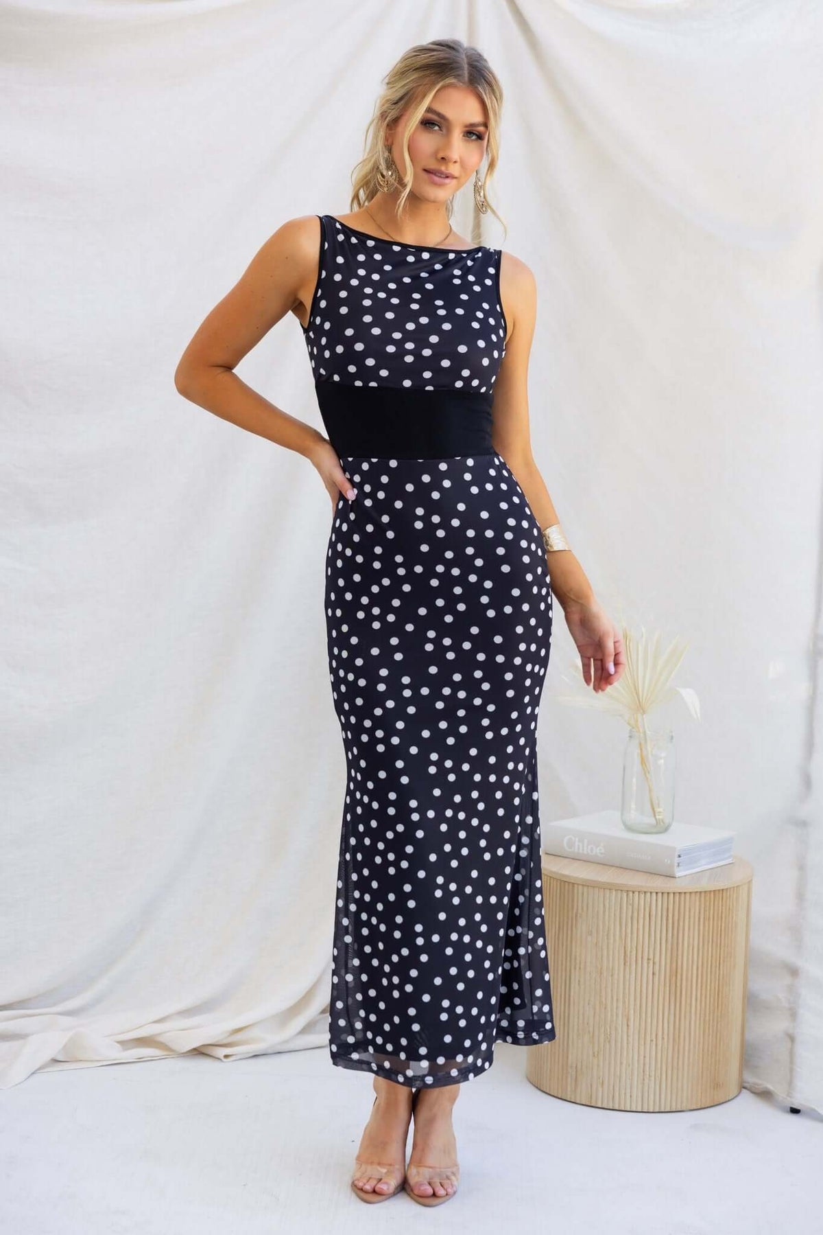 Black maxi dress with polka dots, boat neckline, and fitted silhouette, showcased by model in a stylish setting.