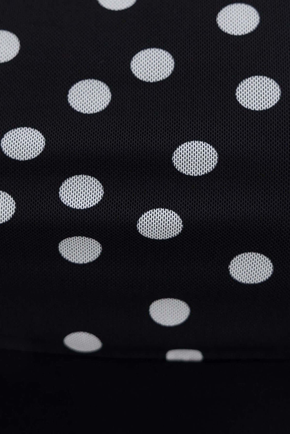 Close-up of black mesh fabric with white polka dots, showcasing its texture and design for fashion apparel.