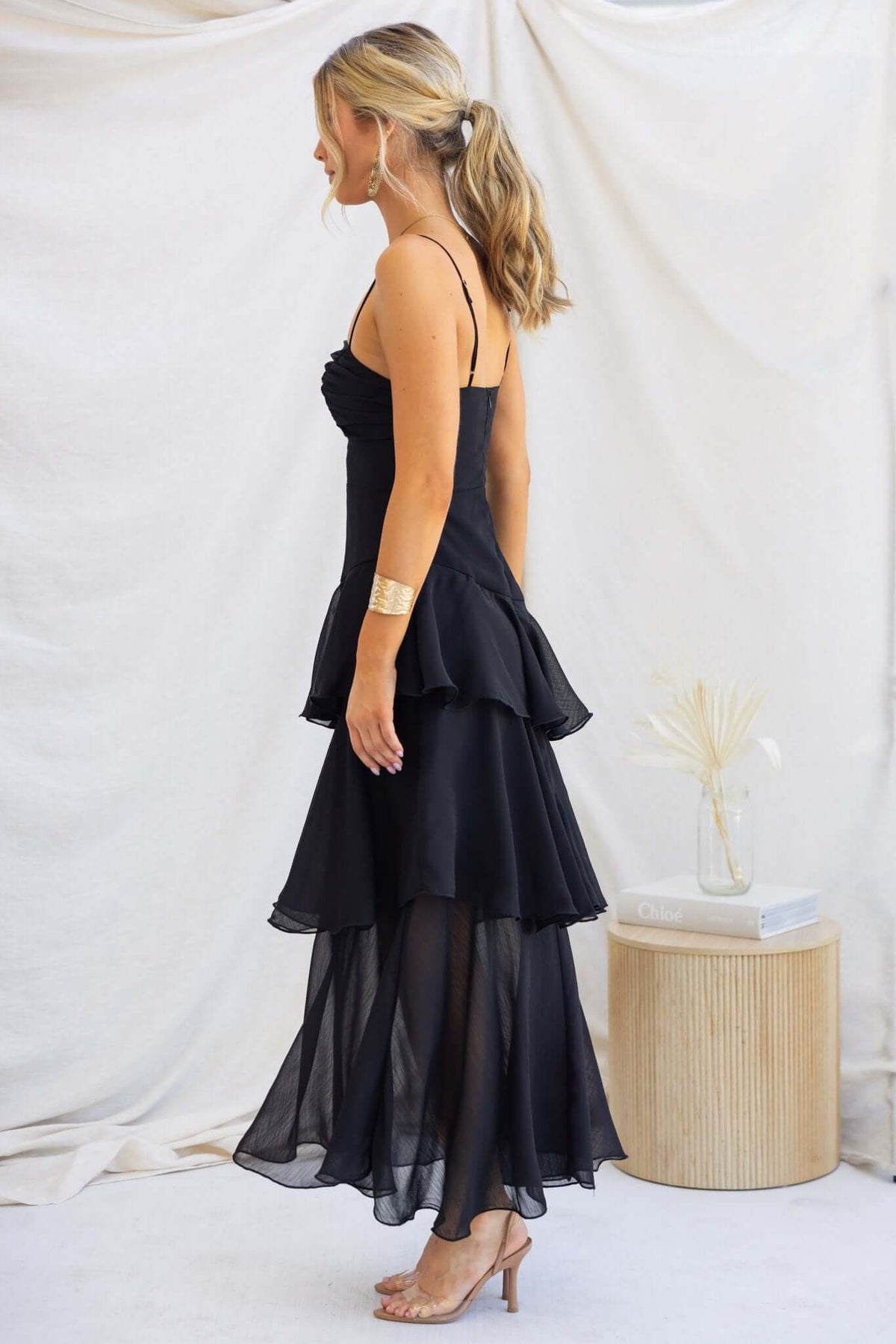 Side view of Saphina Maxi Dress in black with adjustable straps and multi-tier ruffle skirt, styled elegantly.