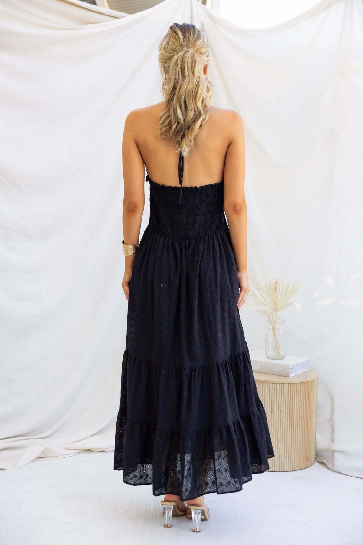 Back view of a woman in a black maxi dress with tie straps, showcasing Anglaise material and tiered design.