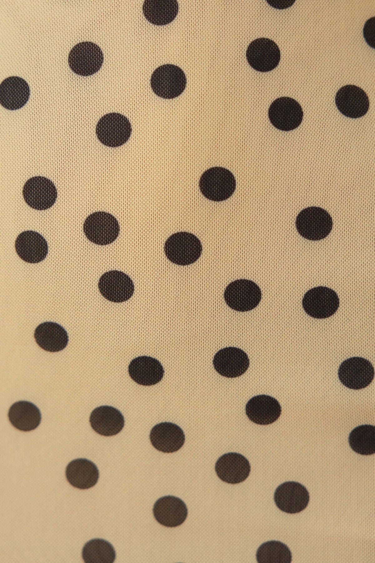 Close-up of beige mesh fabric featuring black polka dots, ideal for stylish dress designs.