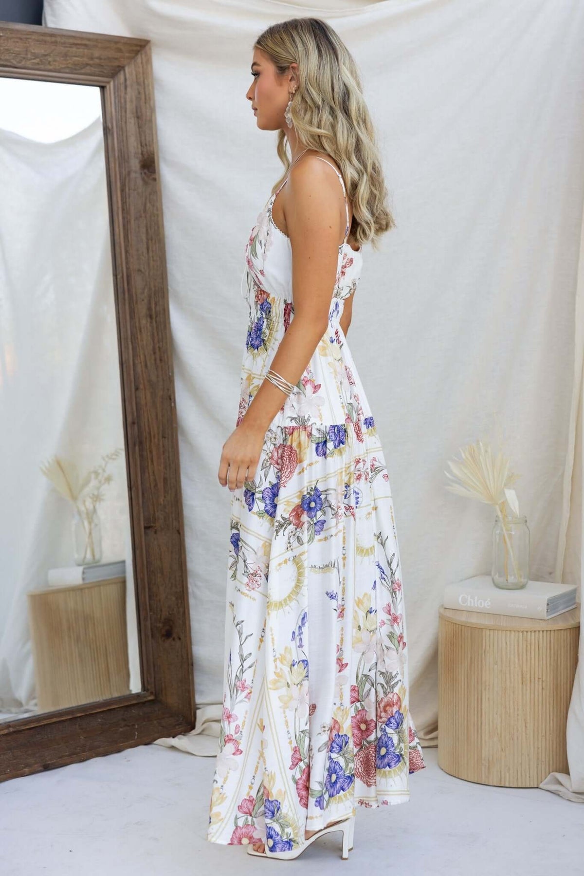 Model wearing Garlyn Maxi Dress with floral design and adjustable straps, side view in a soft, neutral setting.