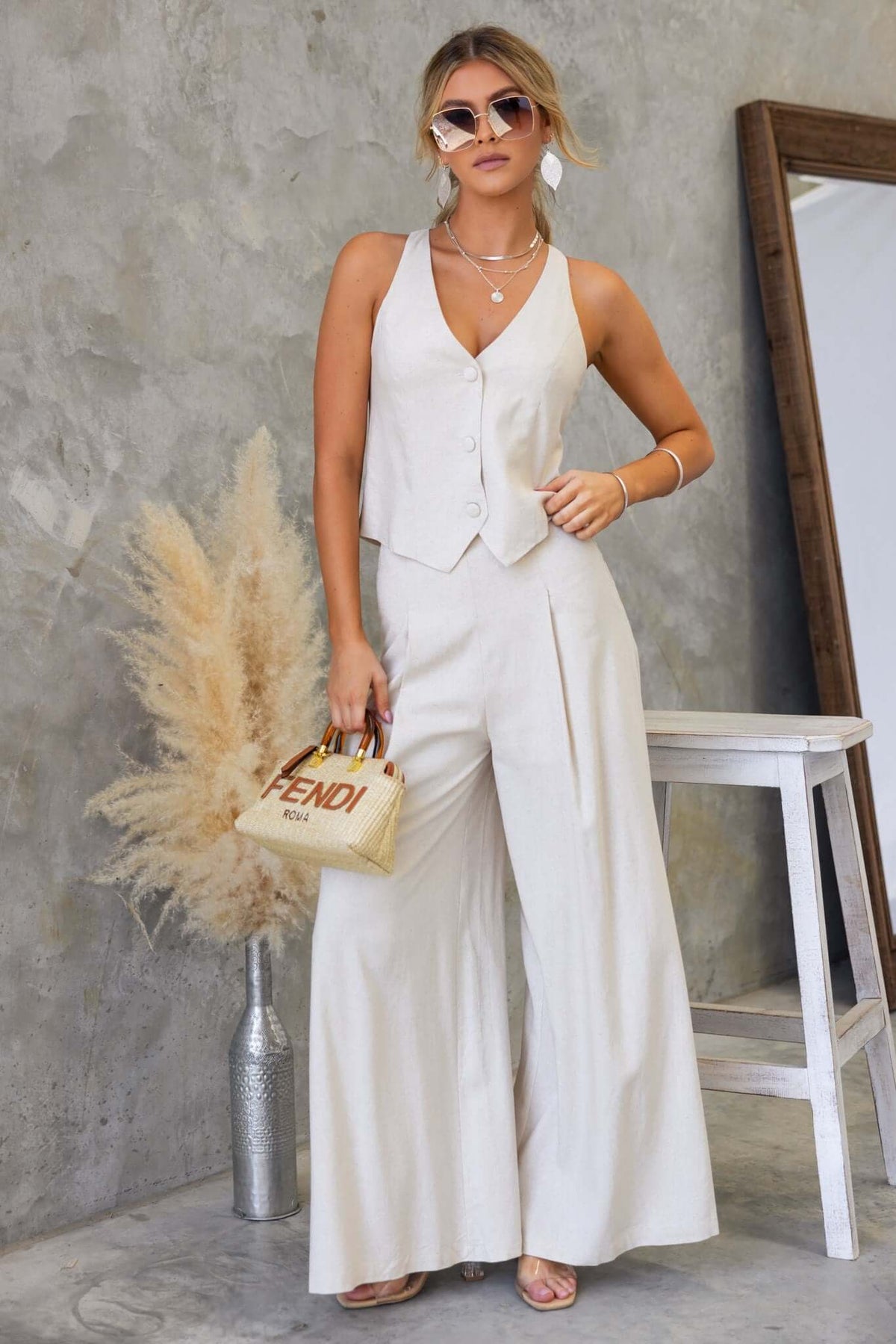 Model wearing Urbanne Set in cream, featuring a button-up vest and wide-leg pants, styled with accessories and sunglasses.