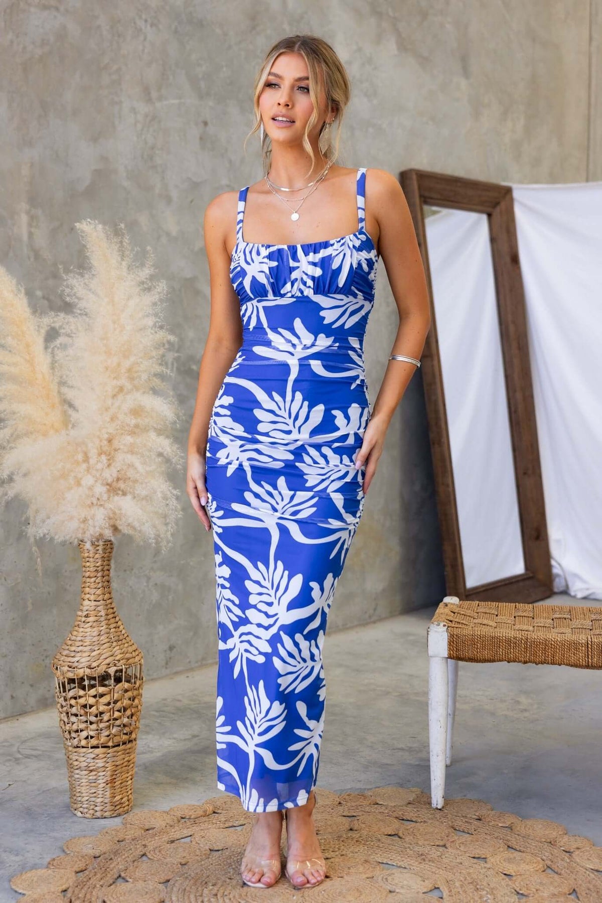 Model wearing a blue floral print maxi dress with adjustable straps, set in a stylish indoor environment.