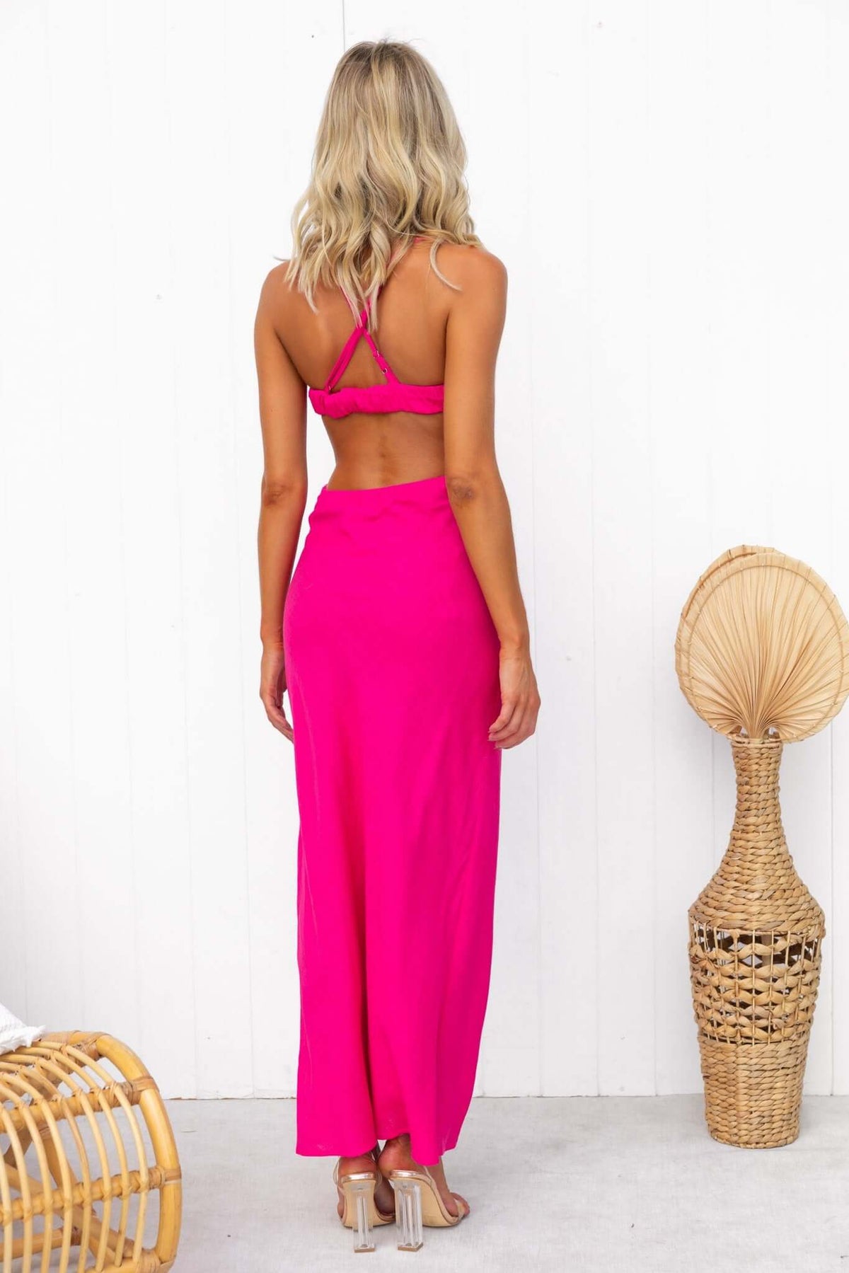 Back view of a woman in a bright pink midi dress with adjustable straps, styled in a minimalist setting.