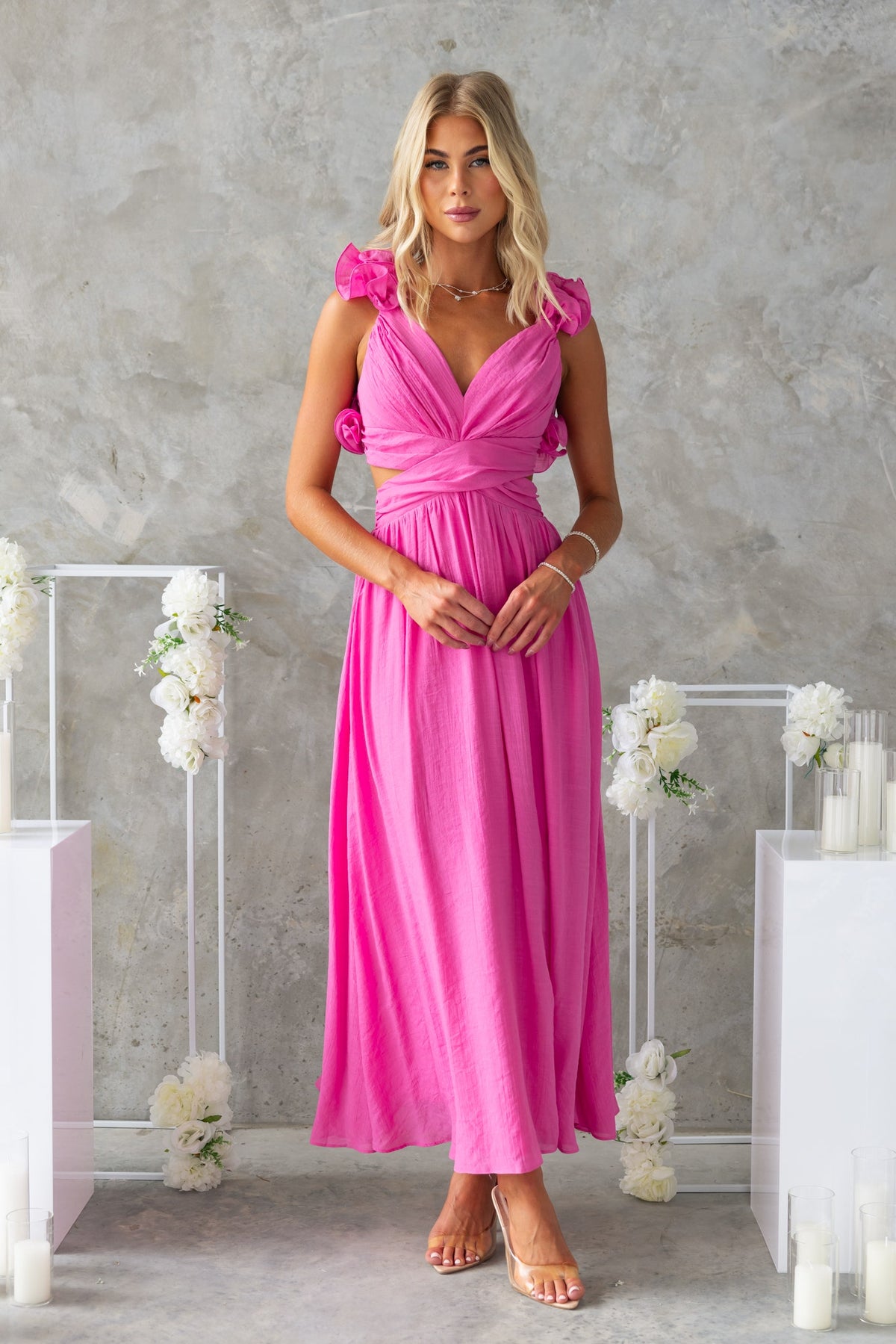 Model wearing a pink Luciana Maxi Dress with ruffle straps, V-neckline, and cut-out waist in a stylish setting.