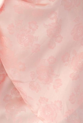 Close-up of soft pink floral fabric, showcasing a satin finish and delicate pattern for elegant dress design.