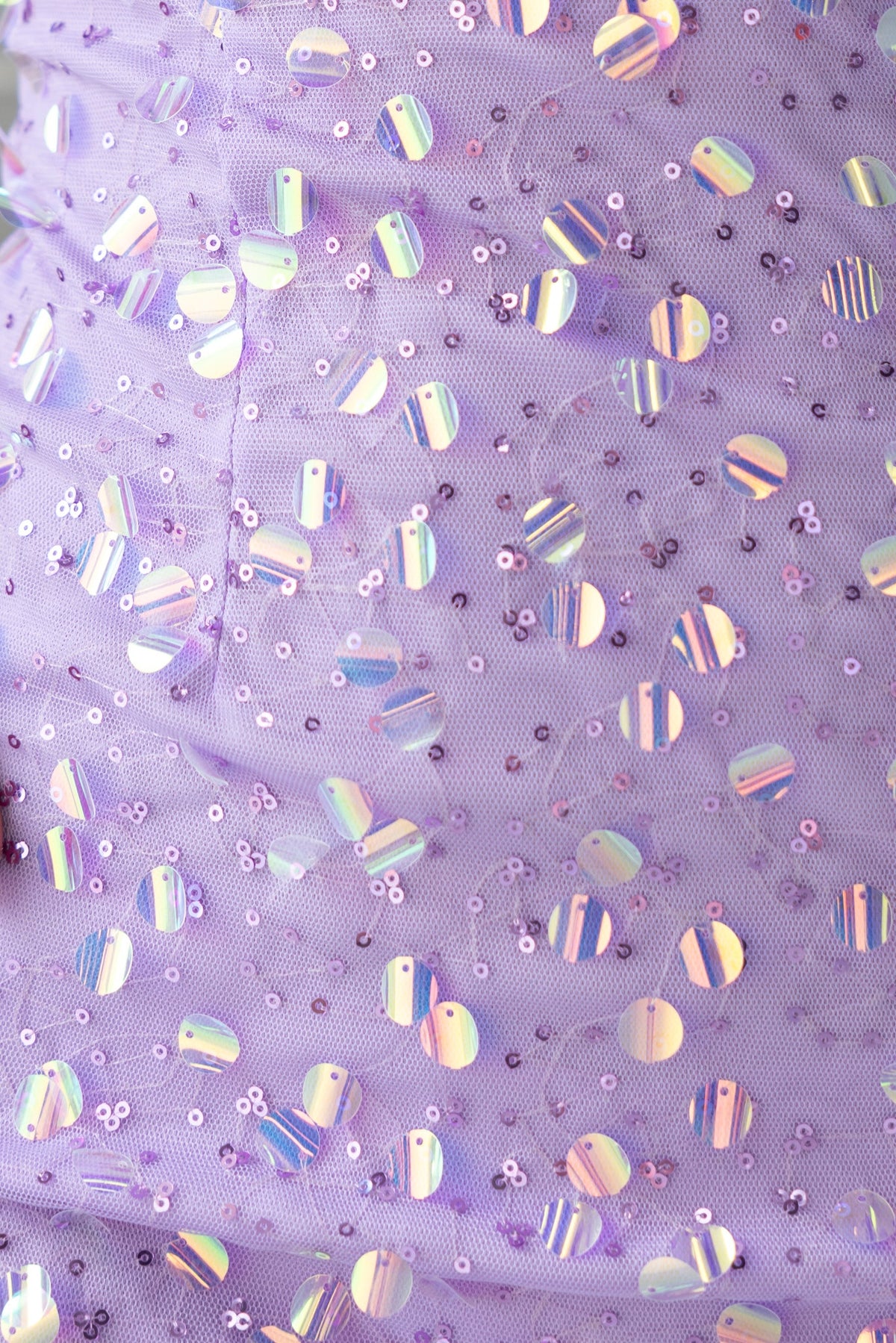 Close-up of purple dress fabric with shimmering sequins and mesh overlay, highlighting texture and detail.