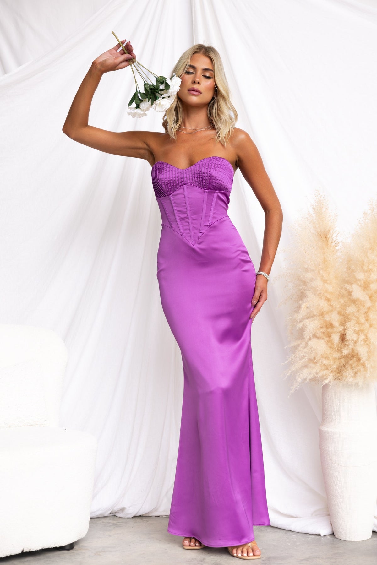 Lars Maxi Dress in vibrant purple, strapless design with boning and satin finish, styled with a flower.