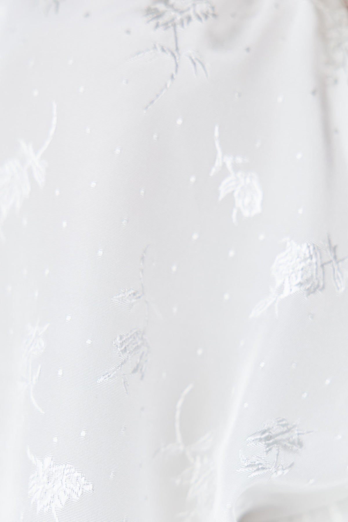 Close-up of delicate floral lace detailing on a sheer white fabric, showcasing intricate patterns and embroidery.