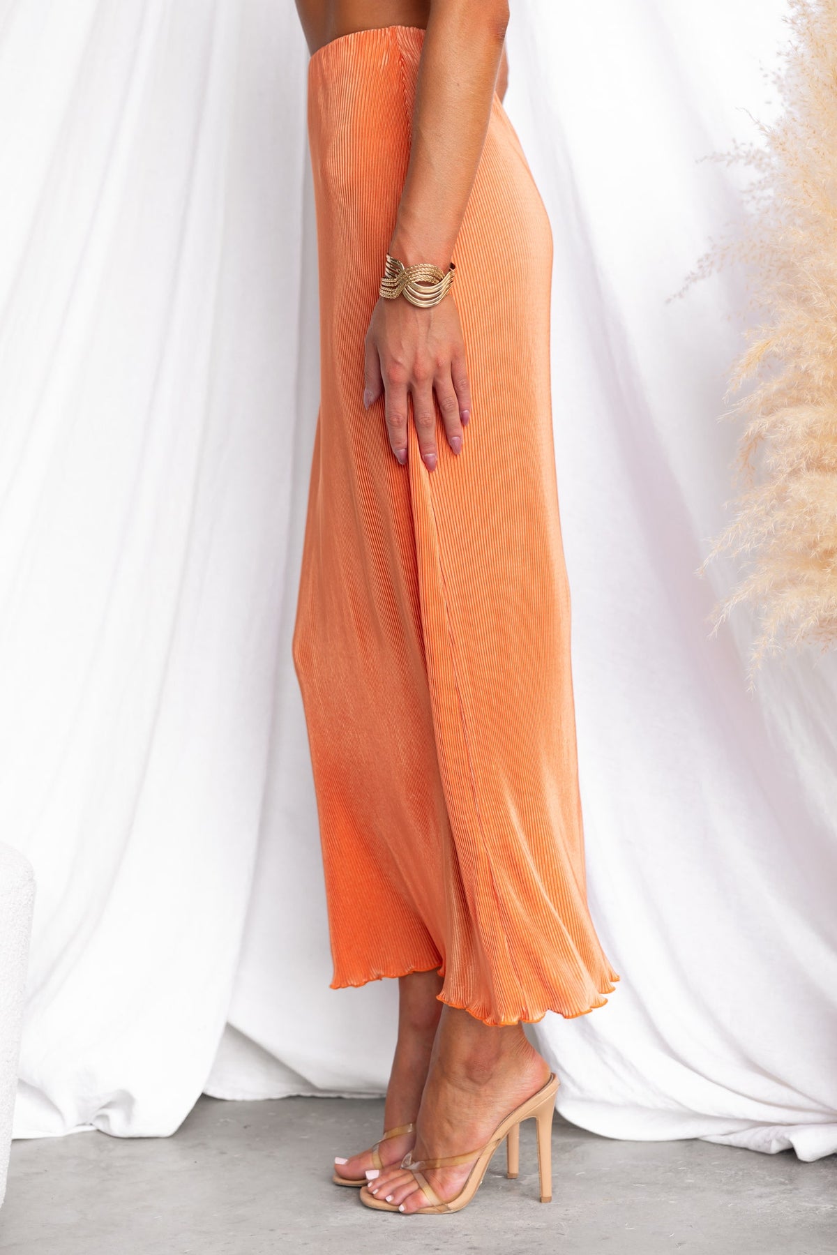 Wondrous maxi skirt in orange with accordion pleats, worn with a stylish bracelet and sandals, against a white backdrop.