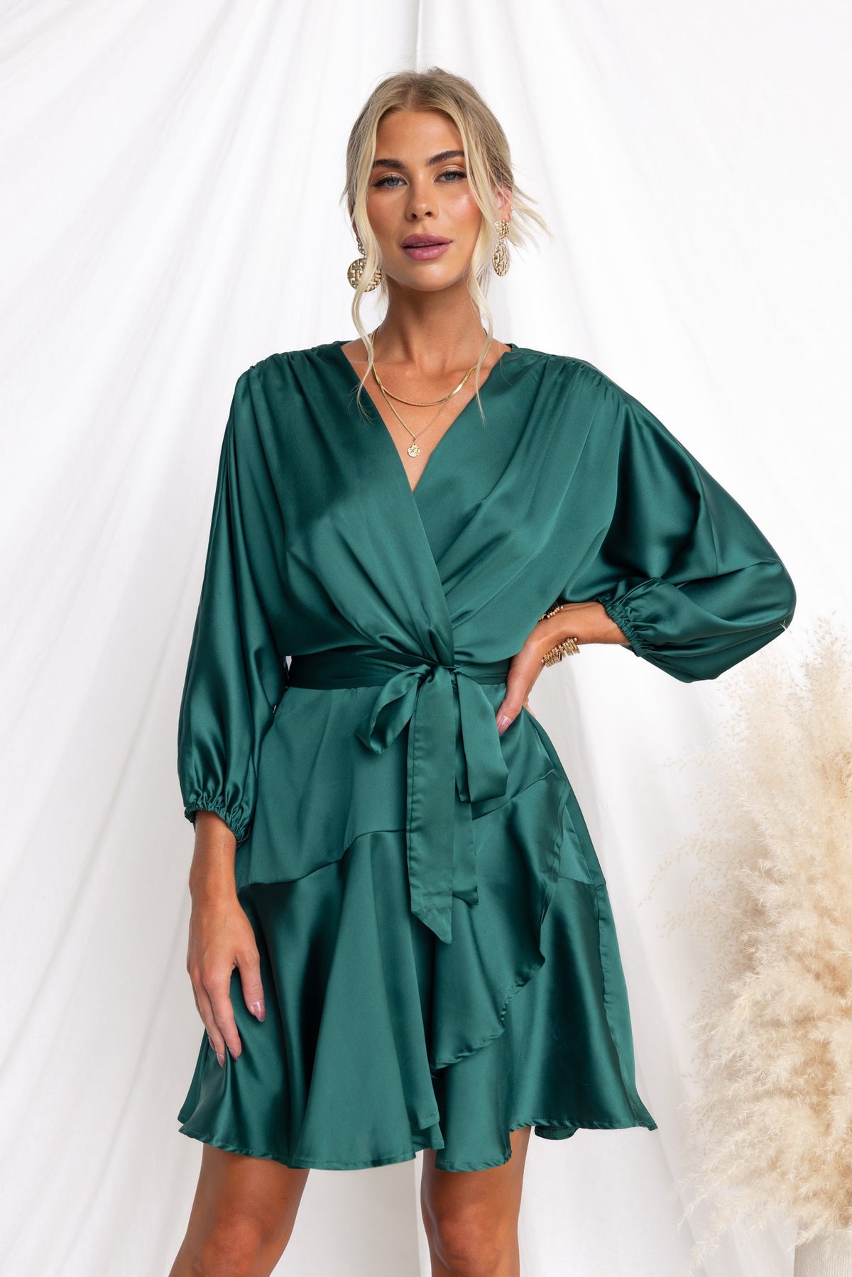 Xention Dress in green satin with V-neck, batwing sleeves, and removable belt, featuring a playful ruffled hemline.
