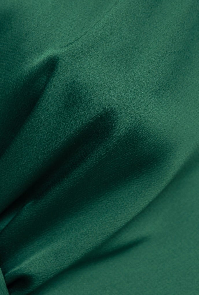 Close-up of luxurious satin fabric in deep green, highlighting soft textures and elegant draping.