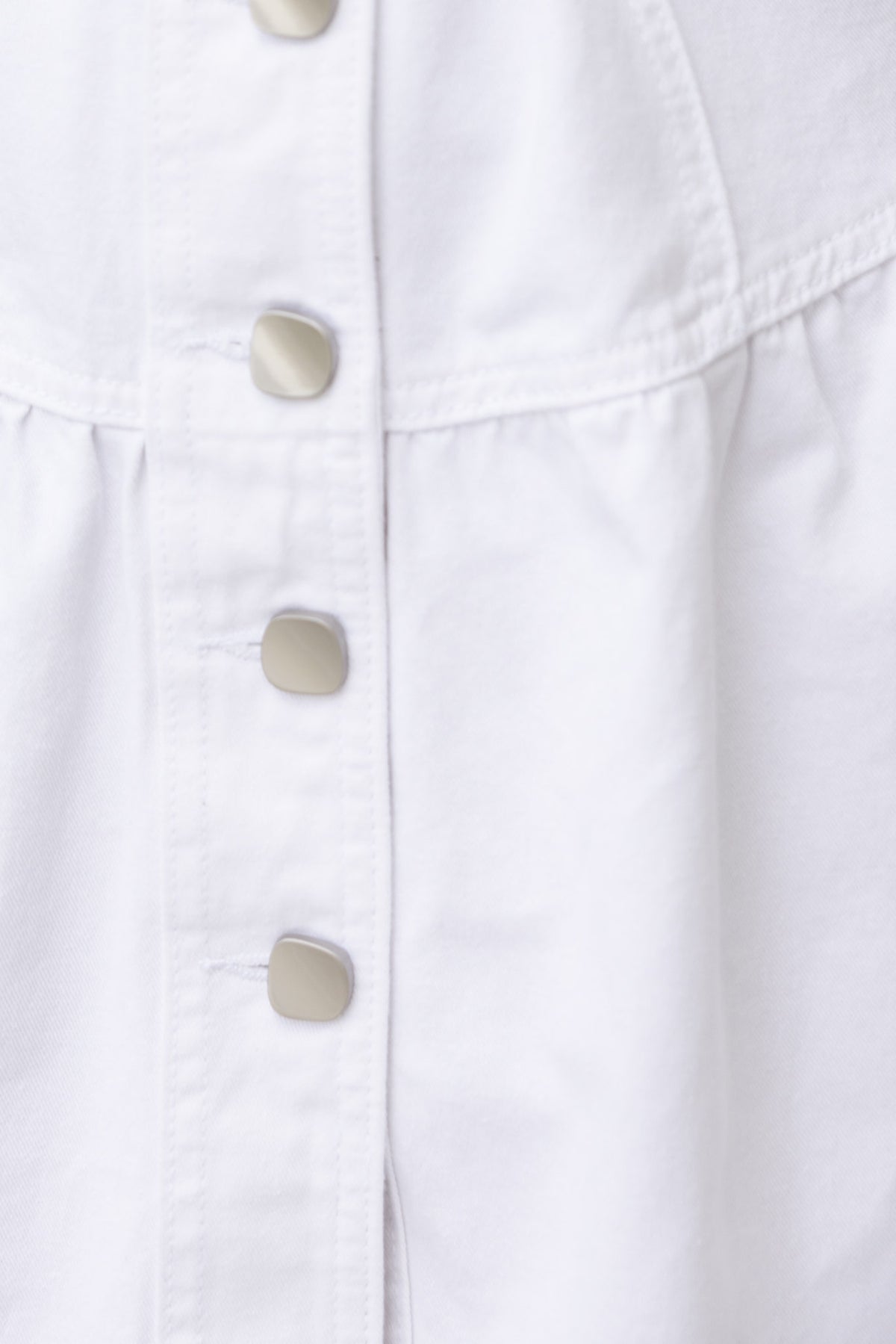 Close-up of a white denim dress featuring a button-up front and gathered waist design.