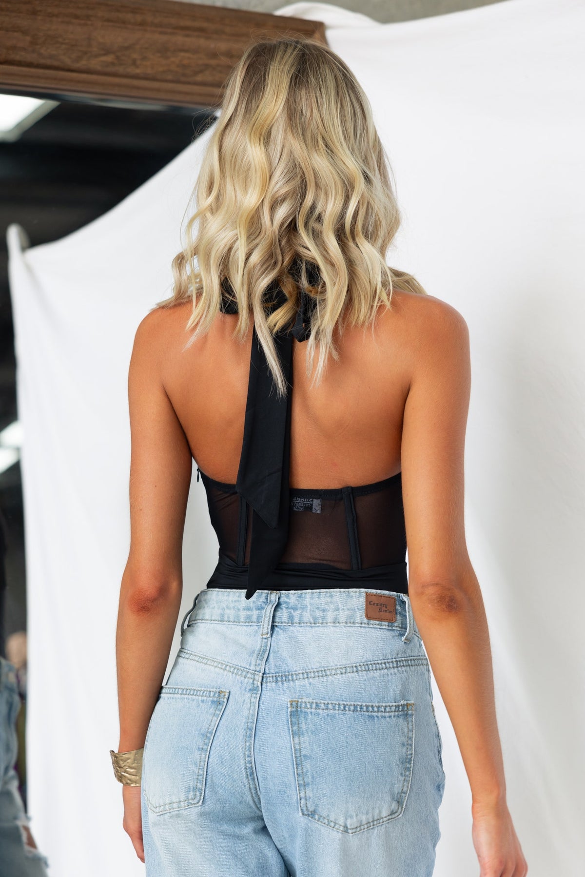 Model wearing Avah Bodysuit from the back, featuring a tie neckline and mesh panel detail.