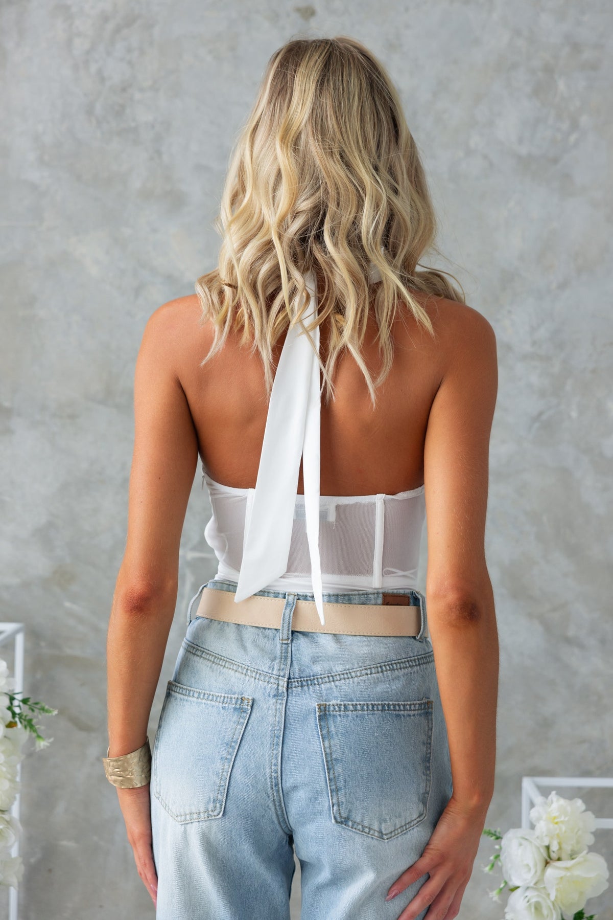 Back view of Avah Bodysuit with adjustable tie neckline, paired with light blue high-waisted jeans.