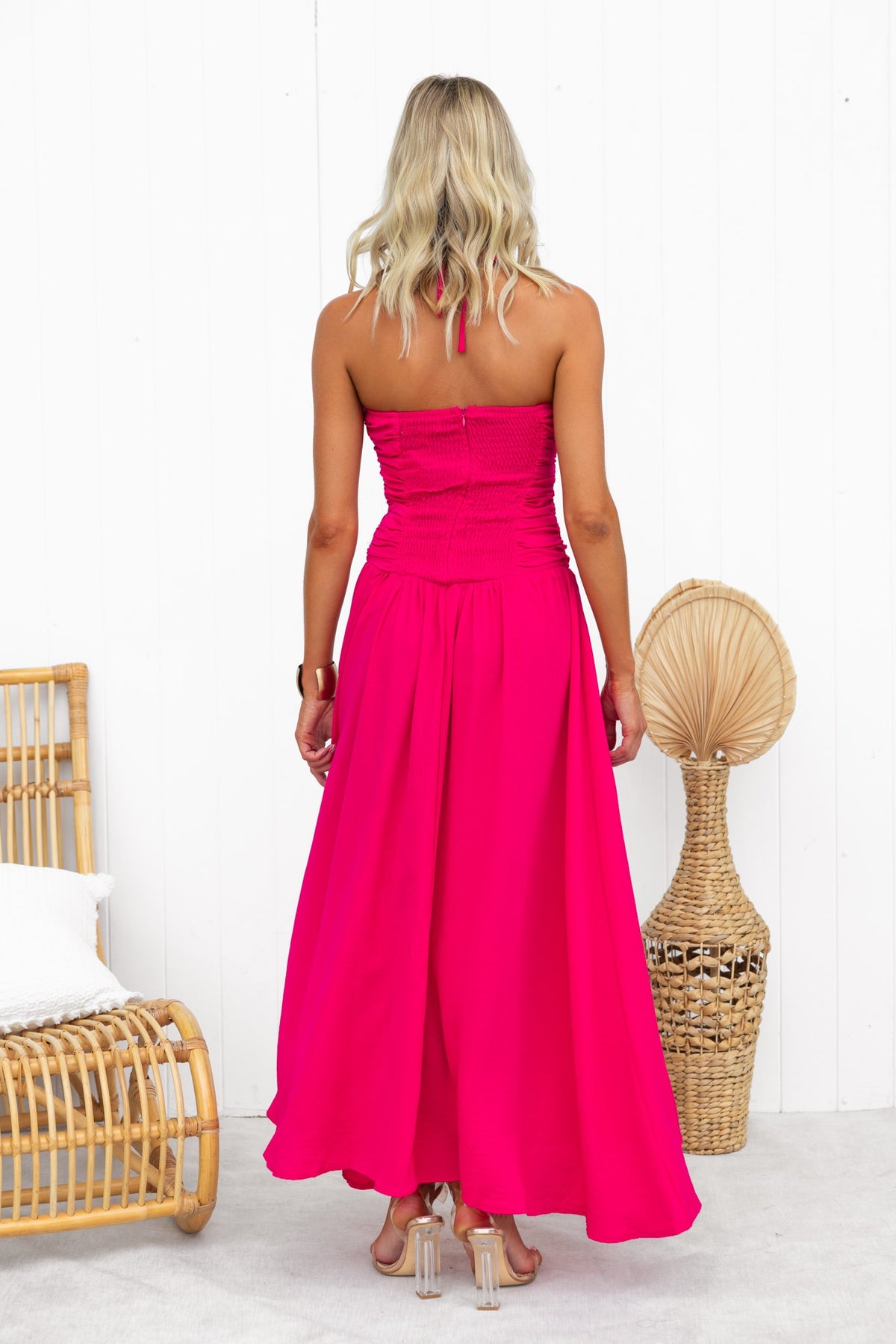 Back view of a woman wearing a vibrant pink Jayma Maxi Dress featuring a ruched bodice and flowing skirt.