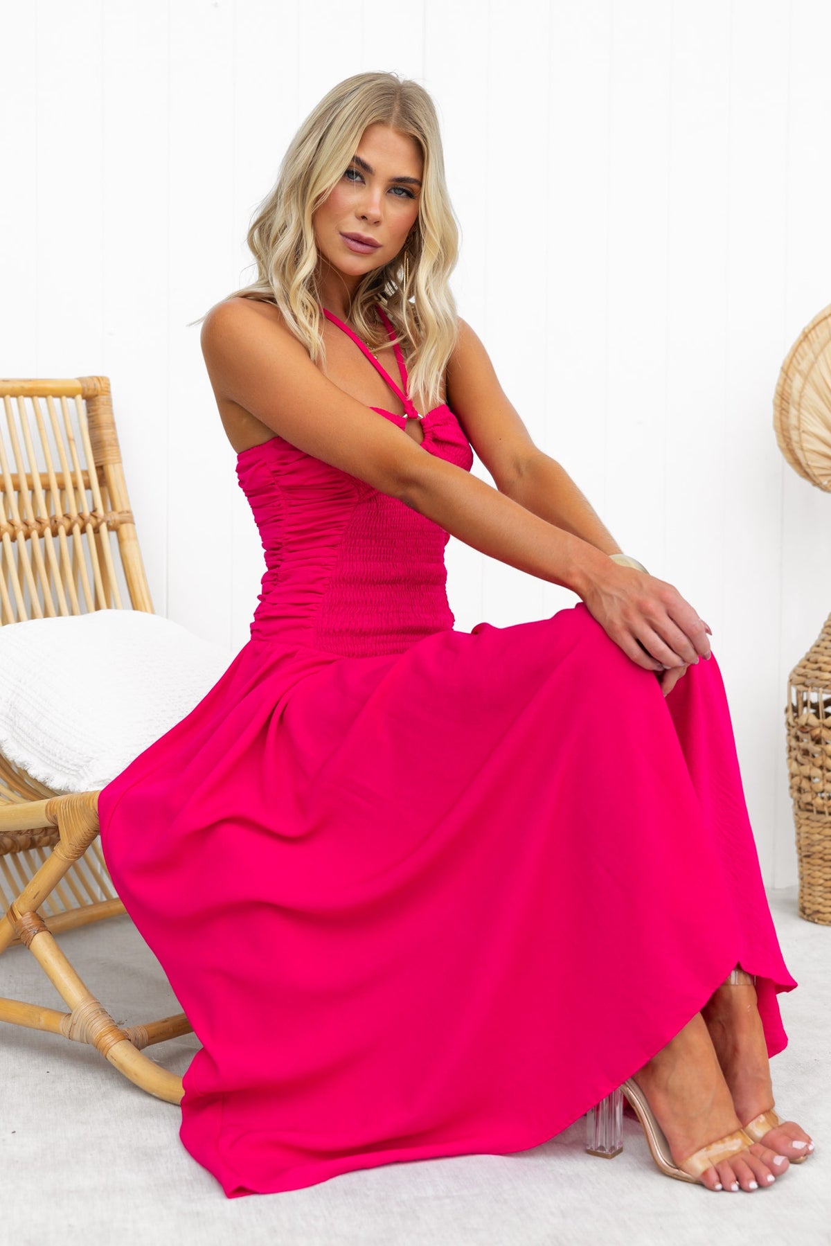 Model wearing a bright pink Jayma Maxi Dress with adjustable neckline and elastic bodice, seated elegantly.