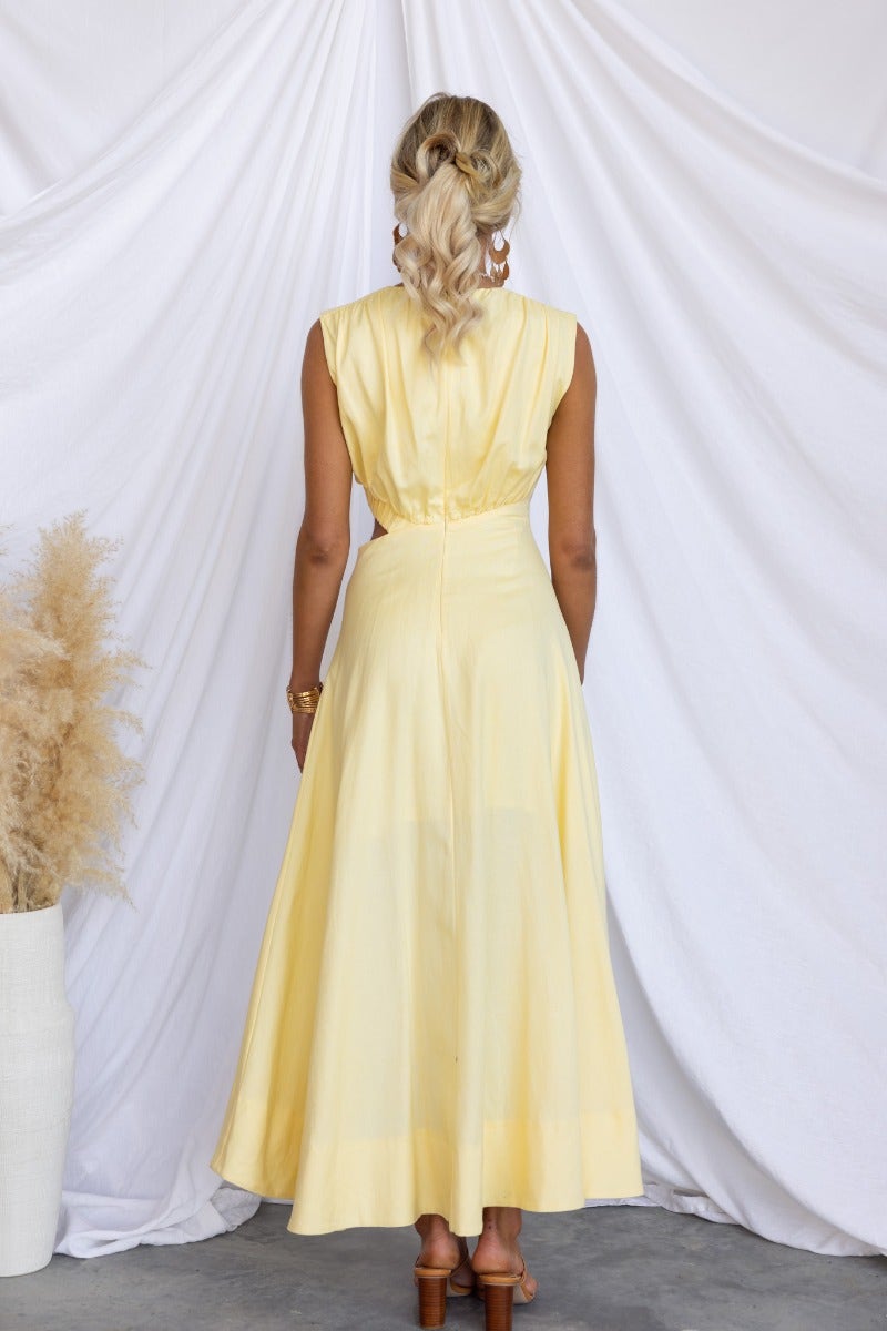 Back view of a woman in a yellow Inspire You maxi dress with a high neckline and elastic waist cut-out.