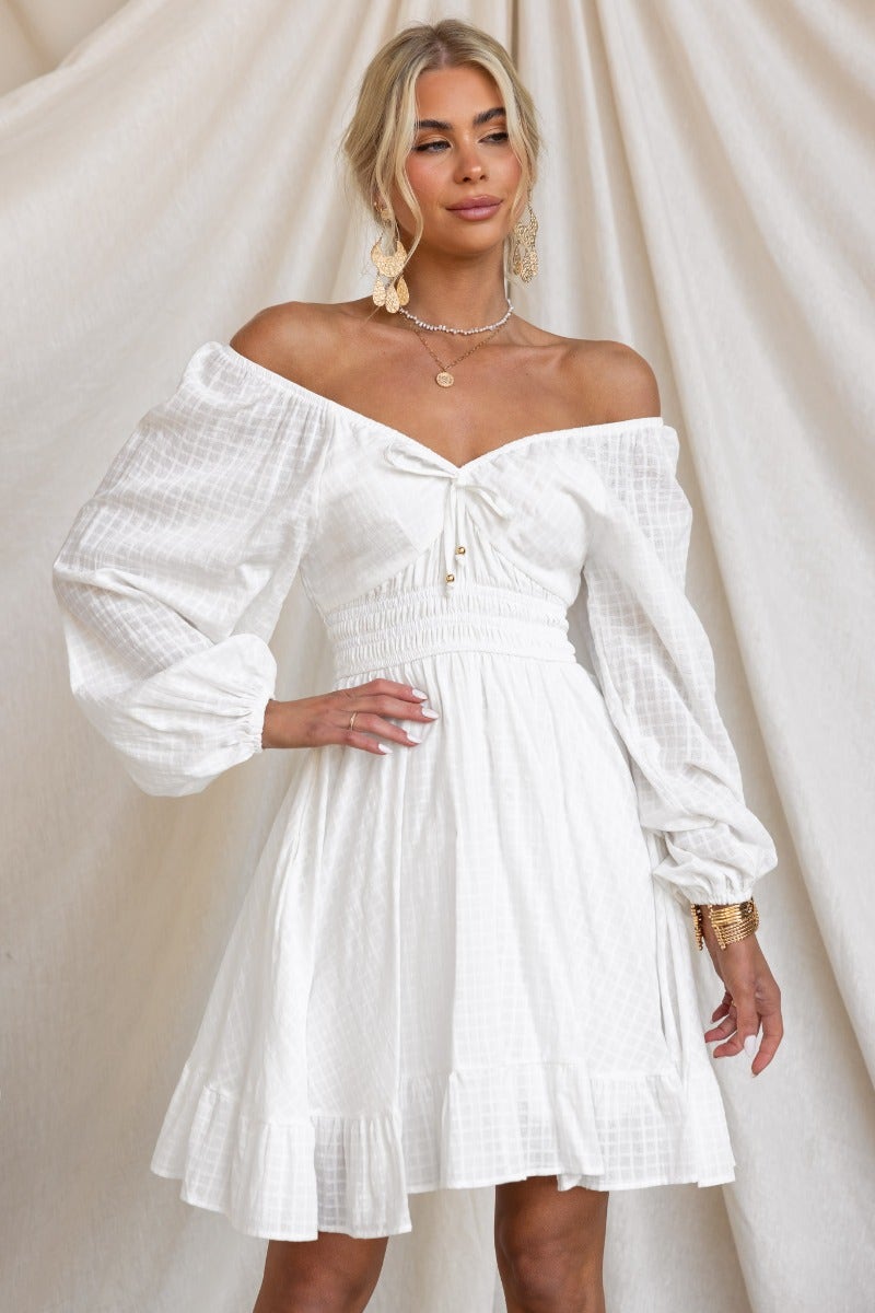 White cotton off-shoulder dress with elastic sleeves, tie detail, and pockets, perfect for casual outings.