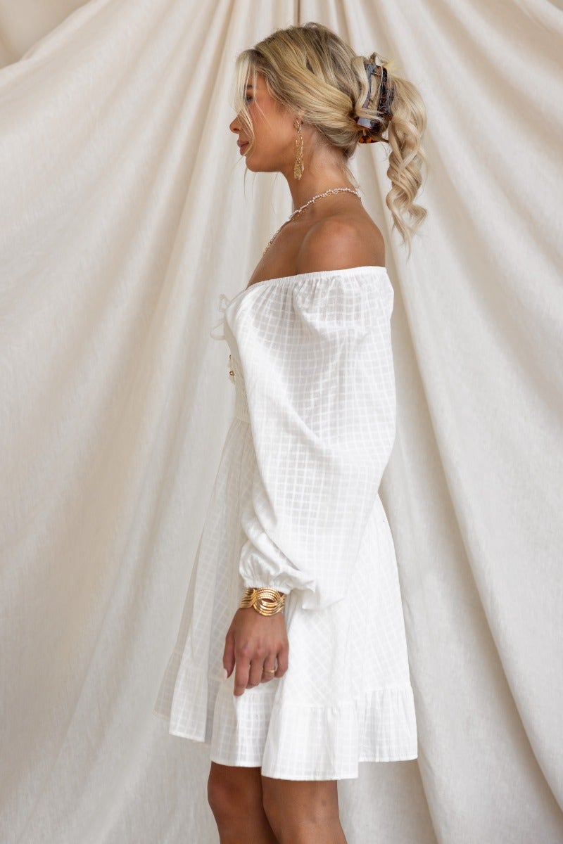 Model side view of the Getaway Dress, a white cotton dress with elastic fitting sleeves and tie detail at neckline.