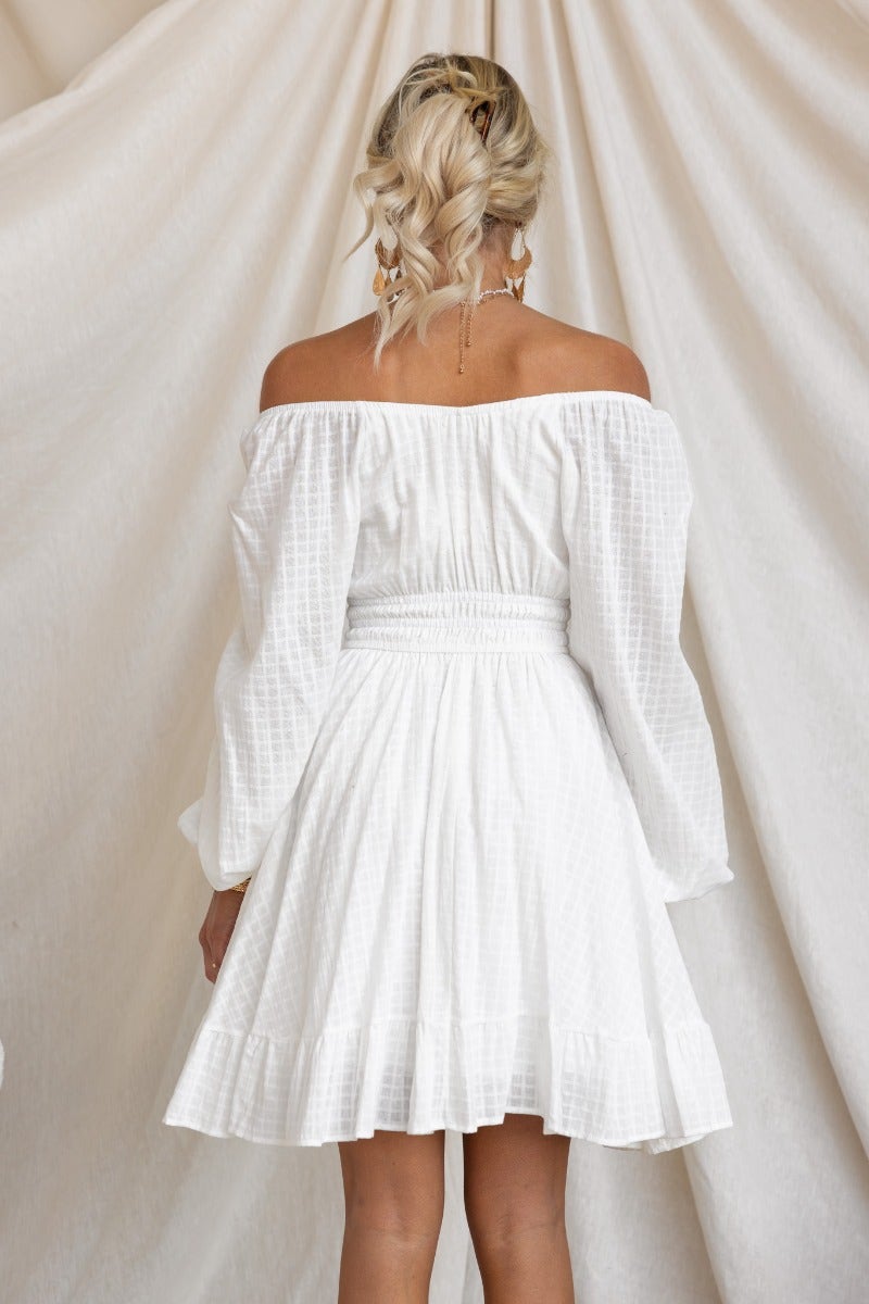 Back view of a women's off-shoulder white cotton dress with long sleeves and a fitted waistband.