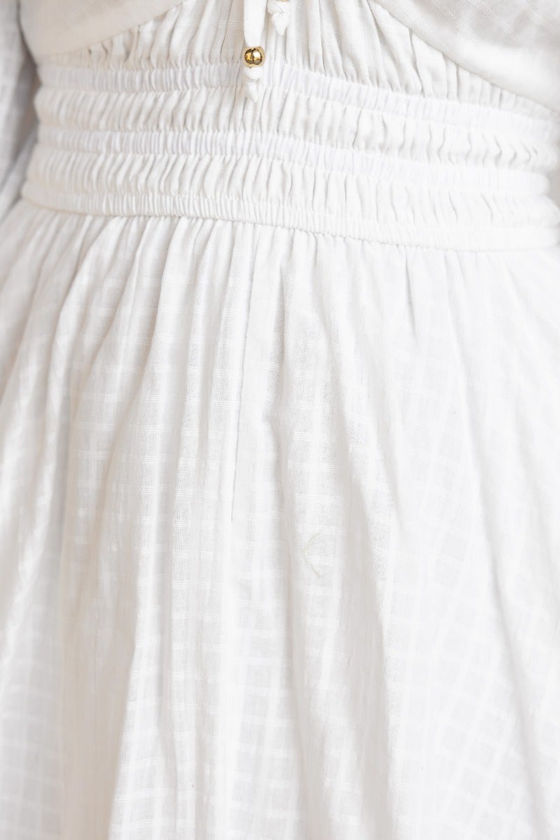 Close-up of the waist area of a white cotton dress with elastic features and decorative gold detail.