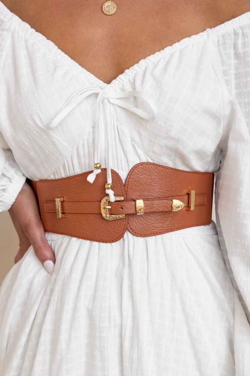 Madden Belt featuring brown leather, gold buckle, and elastic waistband, styled with a white dress.
