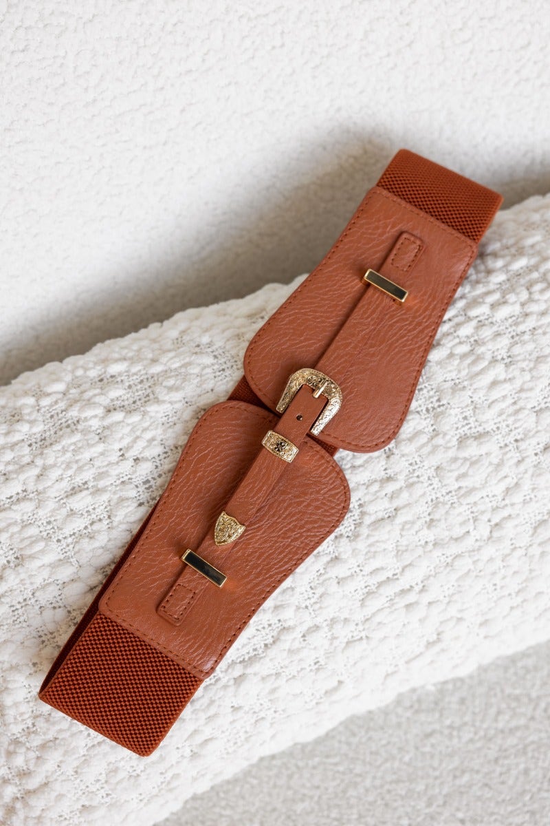 Madden Belt with elastic waistband and gold buckle, showcasing a stylish brown design on textured background.