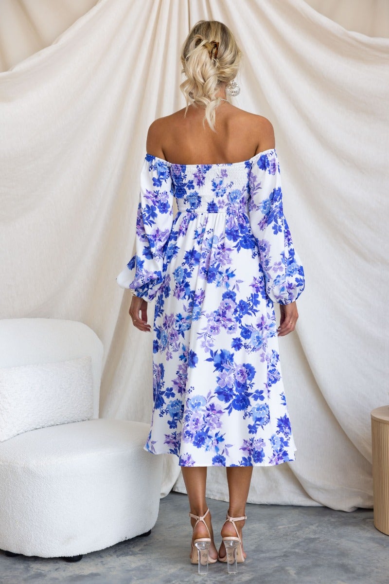 Back view of a woman in a floral midi dress with off-the-shoulder sleeves, displaying blue and white flower patterns.