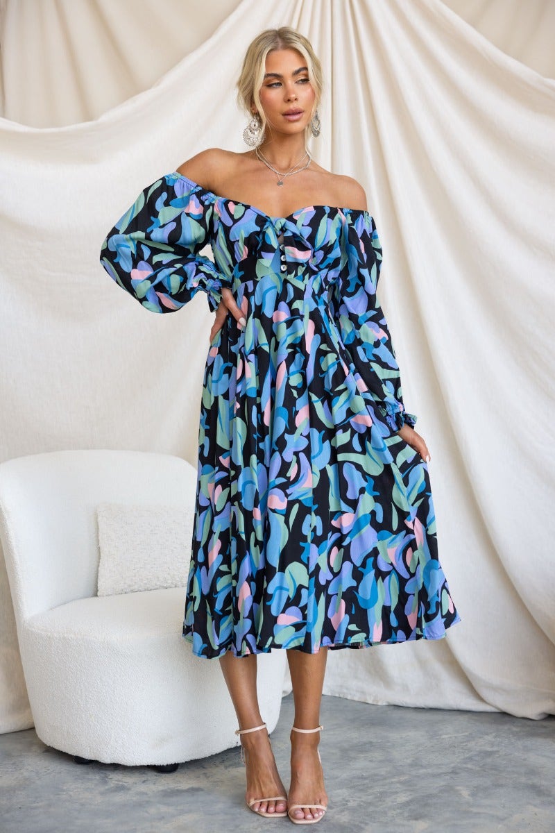 Clemence Midi Dress in black-based print with off-shoulder sleeves and tie detail, styled with heels.