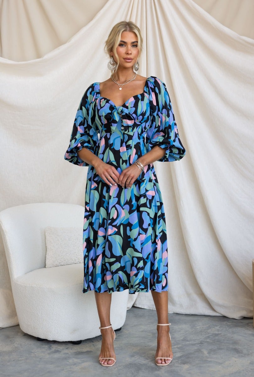 Clemence Midi Dress in colorful print featuring elastic sleeves and tie bust detail, worn by model in stylish setting.