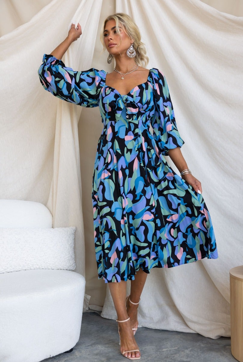 Clemence Midi Dress in a vibrant black-based floral print with puff sleeves and a tie detail at the bust.