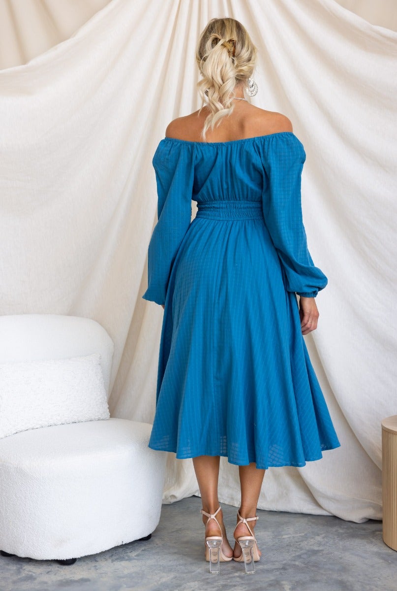 Back view of woman in a blue cotton midi dress with off-shoulder sleeves and tie detail, showcasing its flowy design.
