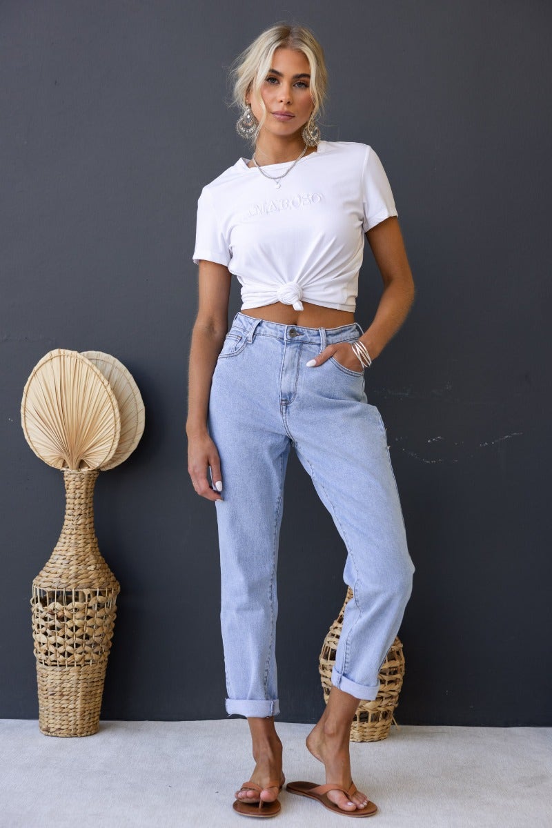 Woman wearing Dori Mom Jeans with mid-high waist and rolled cuffs, styled with a white knotted shirt.