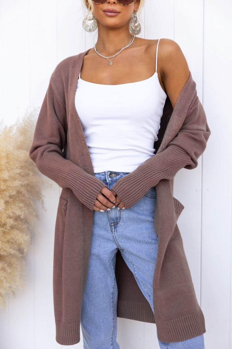 Young woman wearing a brown Motherly Cardigan over a white tank top, styled with light blue jeans.