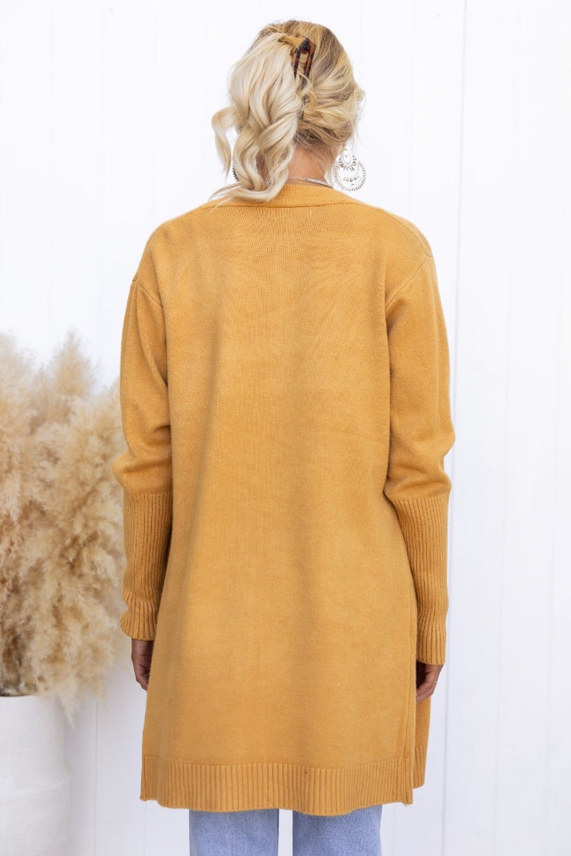 Back view of Motherly Cardigan in mustard color, featuring ribbed knit, longline fit, and pockets.
