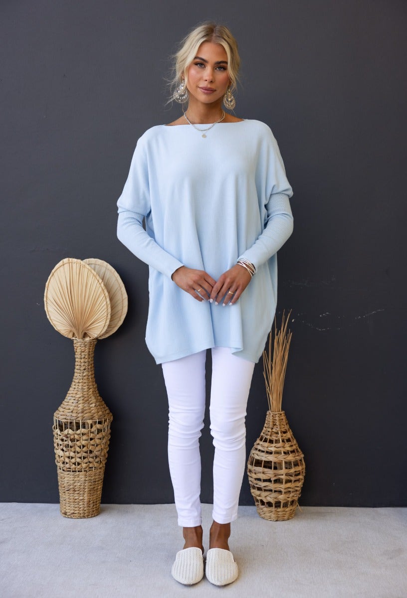 Model wearing oversized Bonnie Knit top in light blue with white jeans, showcasing a cozy and stylish outfit.