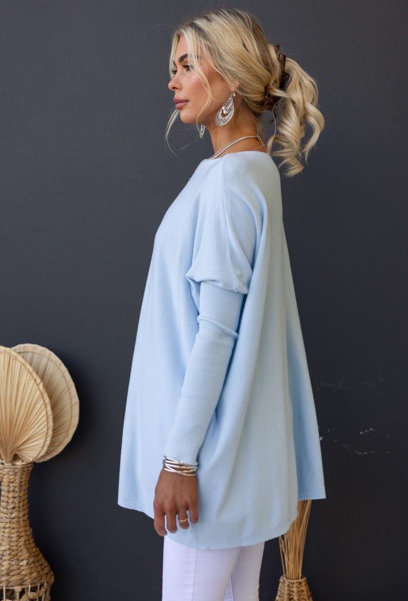 Woman in oversized blue Bonnie Knit top with full-length sleeves, styled with white pants and accessories.
