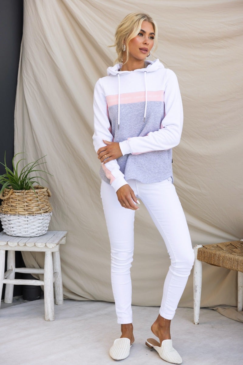 Xarles jumper hoodie in grey with pink stripes, worn with white jeans, featuring a scoop hemline and drawstring hood.