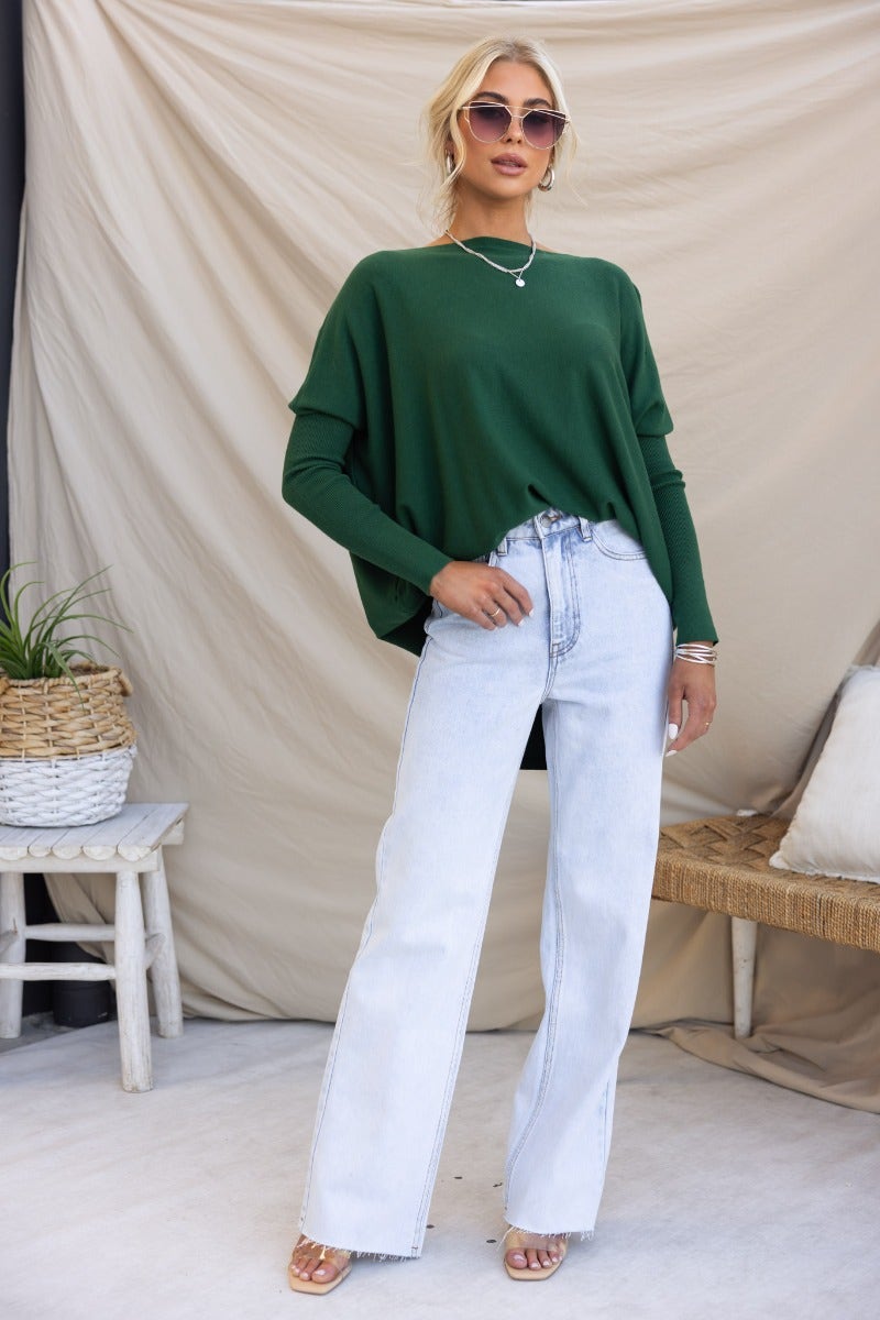 Woman in oversized green knit top and light jeans, showcasing a trendy casual outfit.