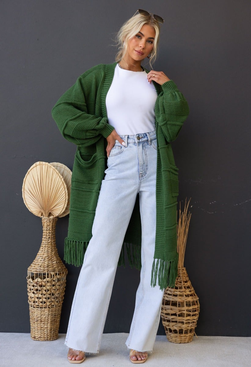 Model wearing a longline green Zeddie cardigan with pockets, paired with high-waisted jeans and a white top.