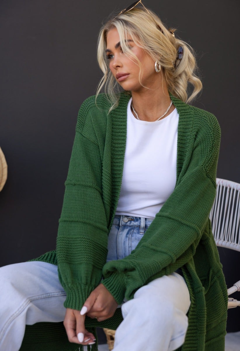 Model wearing a green Zeddie Cardigan over a white shirt, styled with high-waisted jeans.