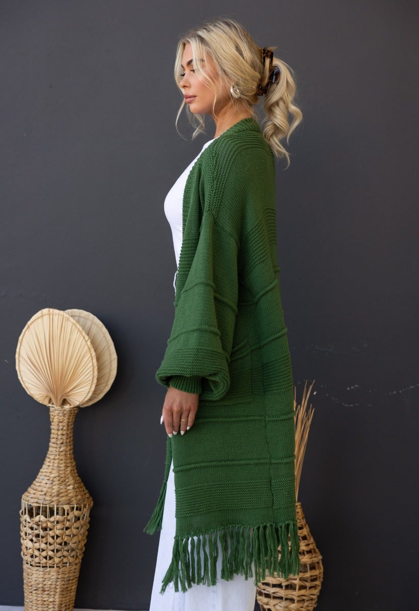 Model wearing a green Zeddie cardigan with fringe detail, styled elegantly against a dark backdrop.