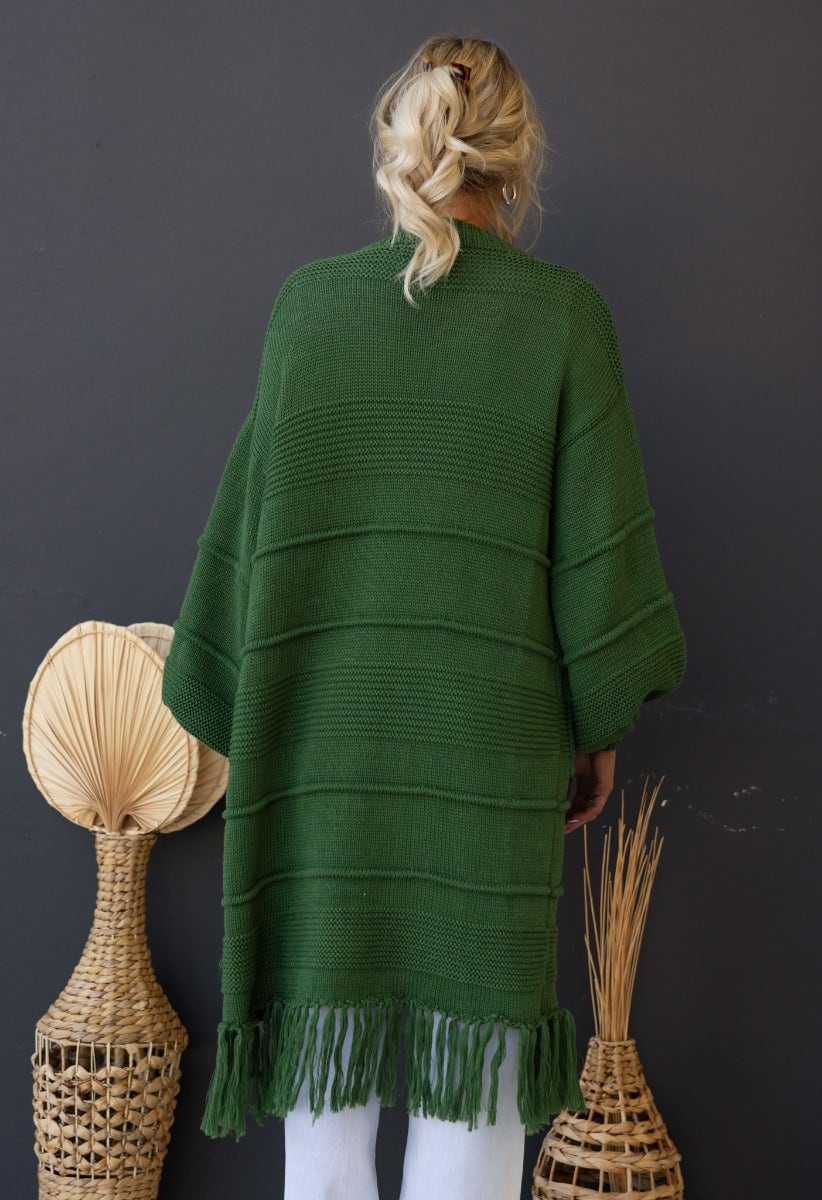 Back view of a longline green knit cardigan with fringe, showcasing relaxed fit and stylish design.