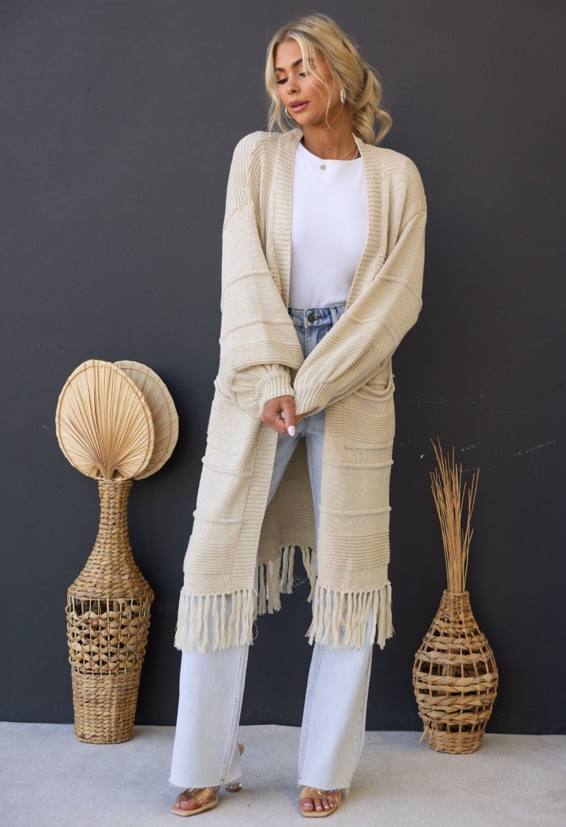 Zeddie Cardigan in cream color, longline fit with pockets, styled with flared jeans and heels, set in a modern decor.