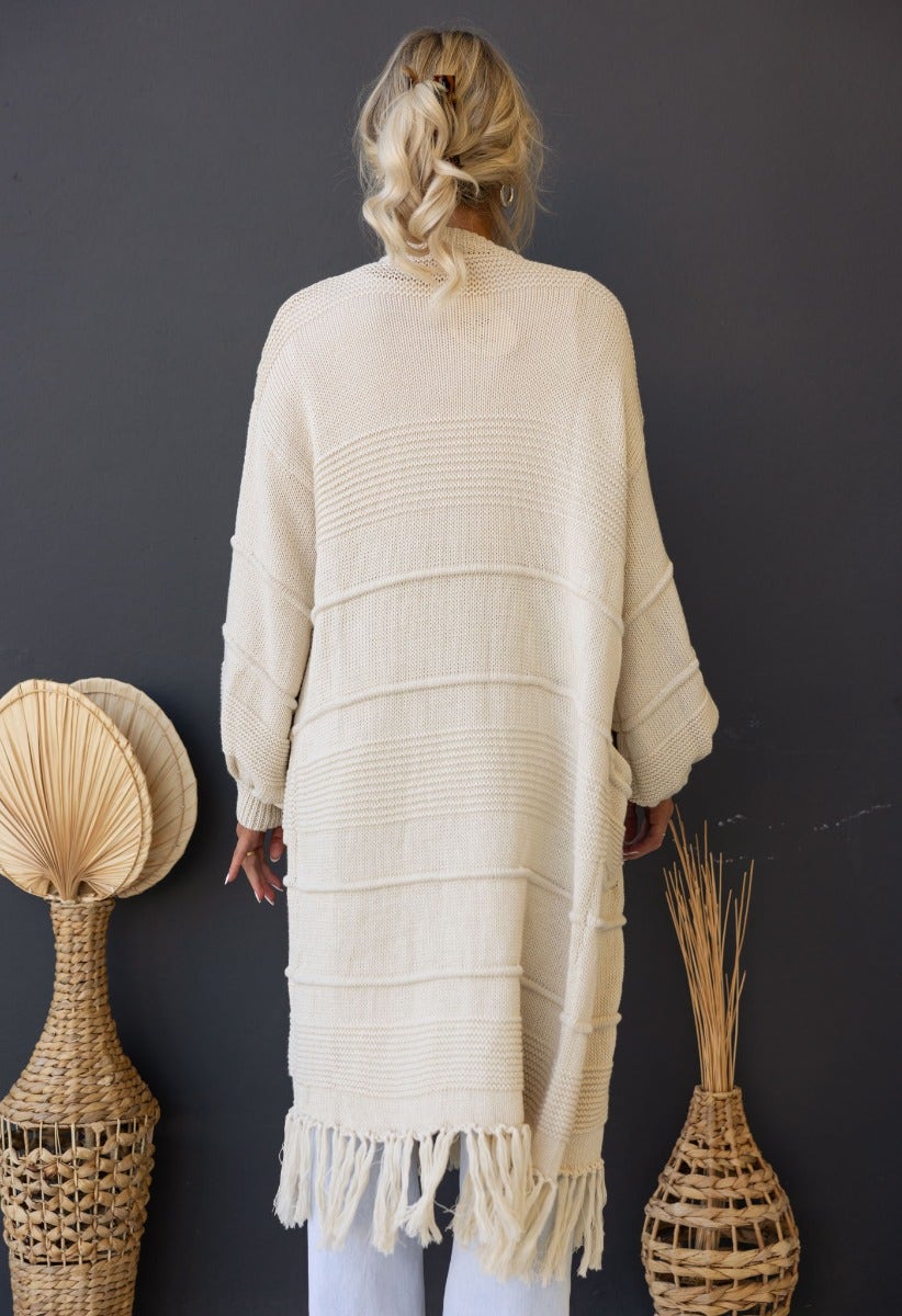 Back view of Zeddie Cardigan, a longline knit cardigan in cream color with stylish fringe detailing.