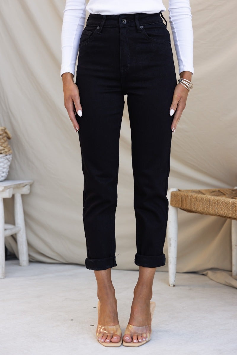 Black mid-high waist Rueben Mom Jeans with rolled cuffs, styled with a long-sleeve top and heels.