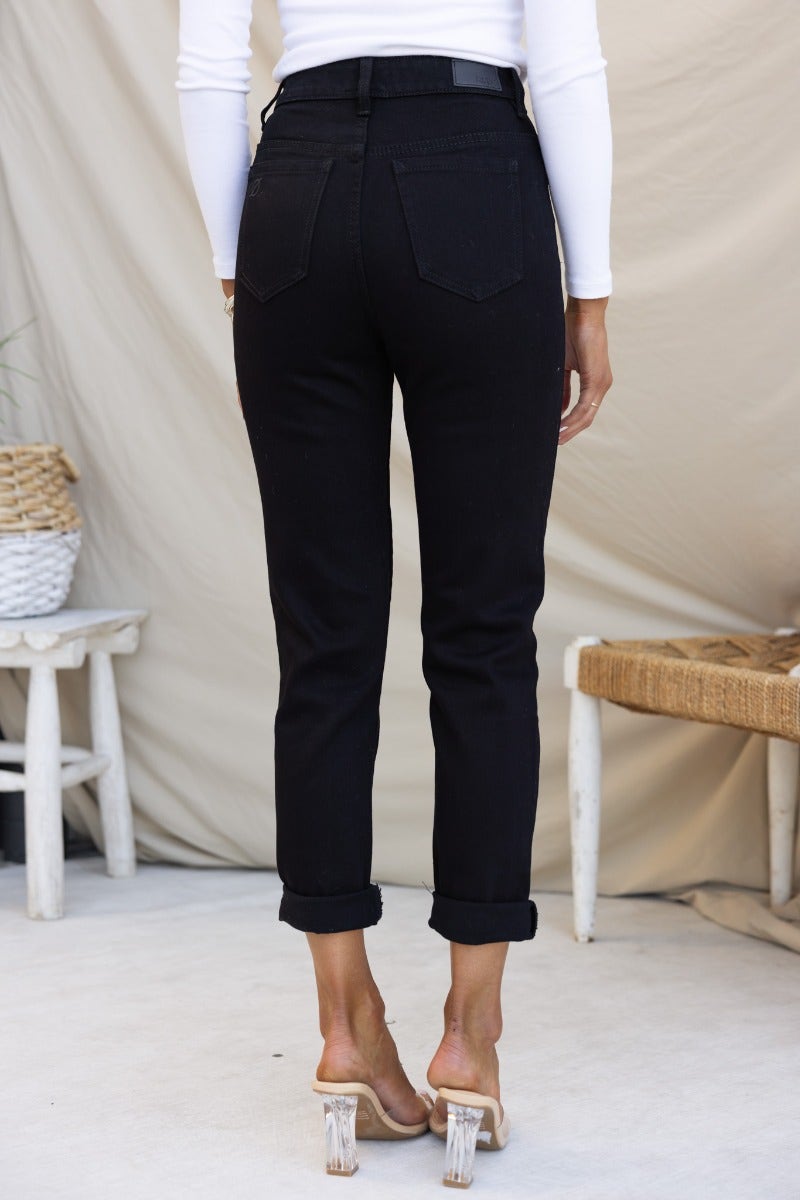 Back view of Rueben Mom Jeans, black denim with mid-high waist and rolled cuffs, showing pockets and a fitted look.